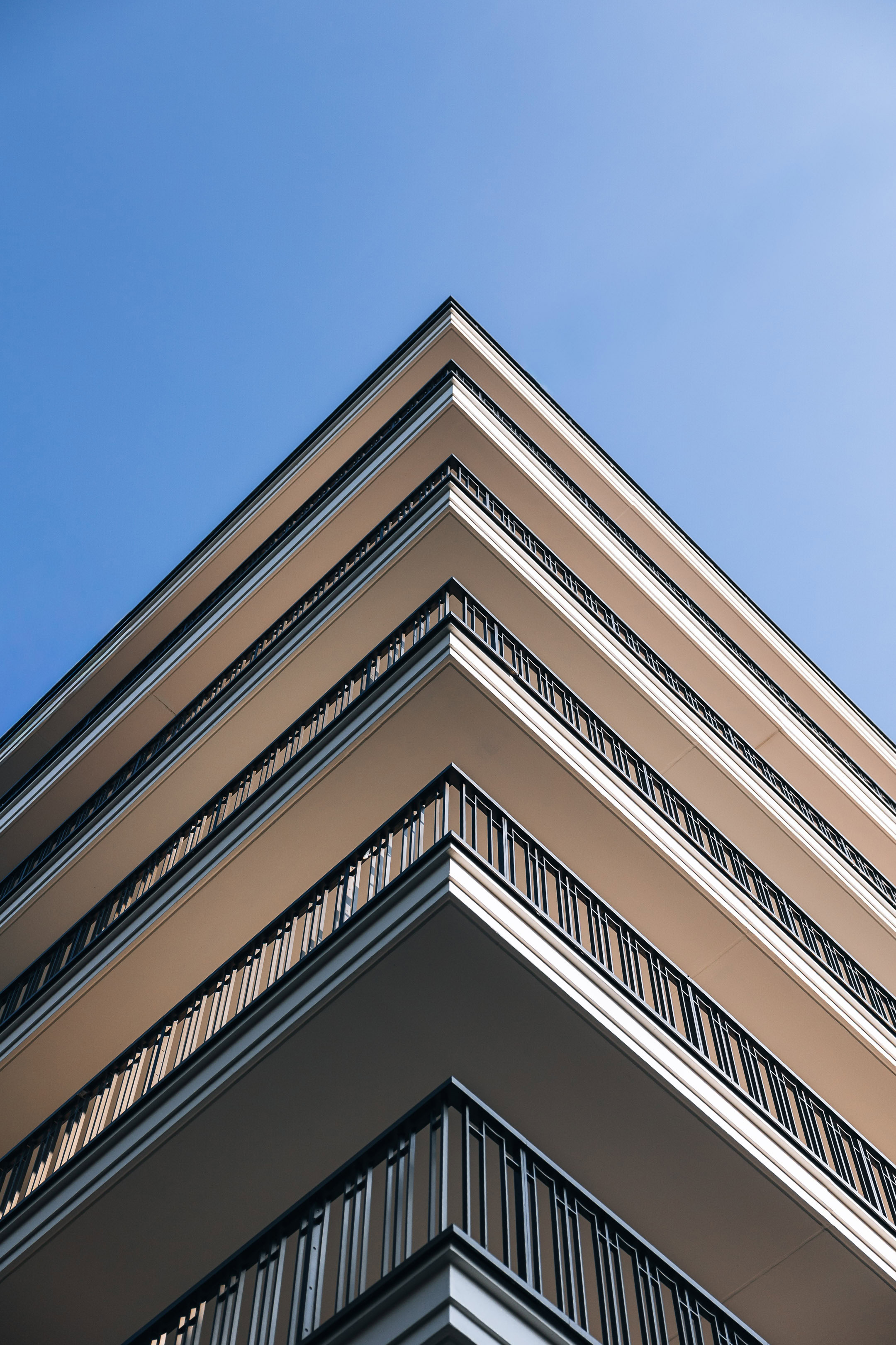 Contre-plong&eacute;e architecturale d'un immeuble de standing avec balcons en angle et garde-corps travaill&eacute;s sur fond de ciel bleu par maxime decarsin photographe