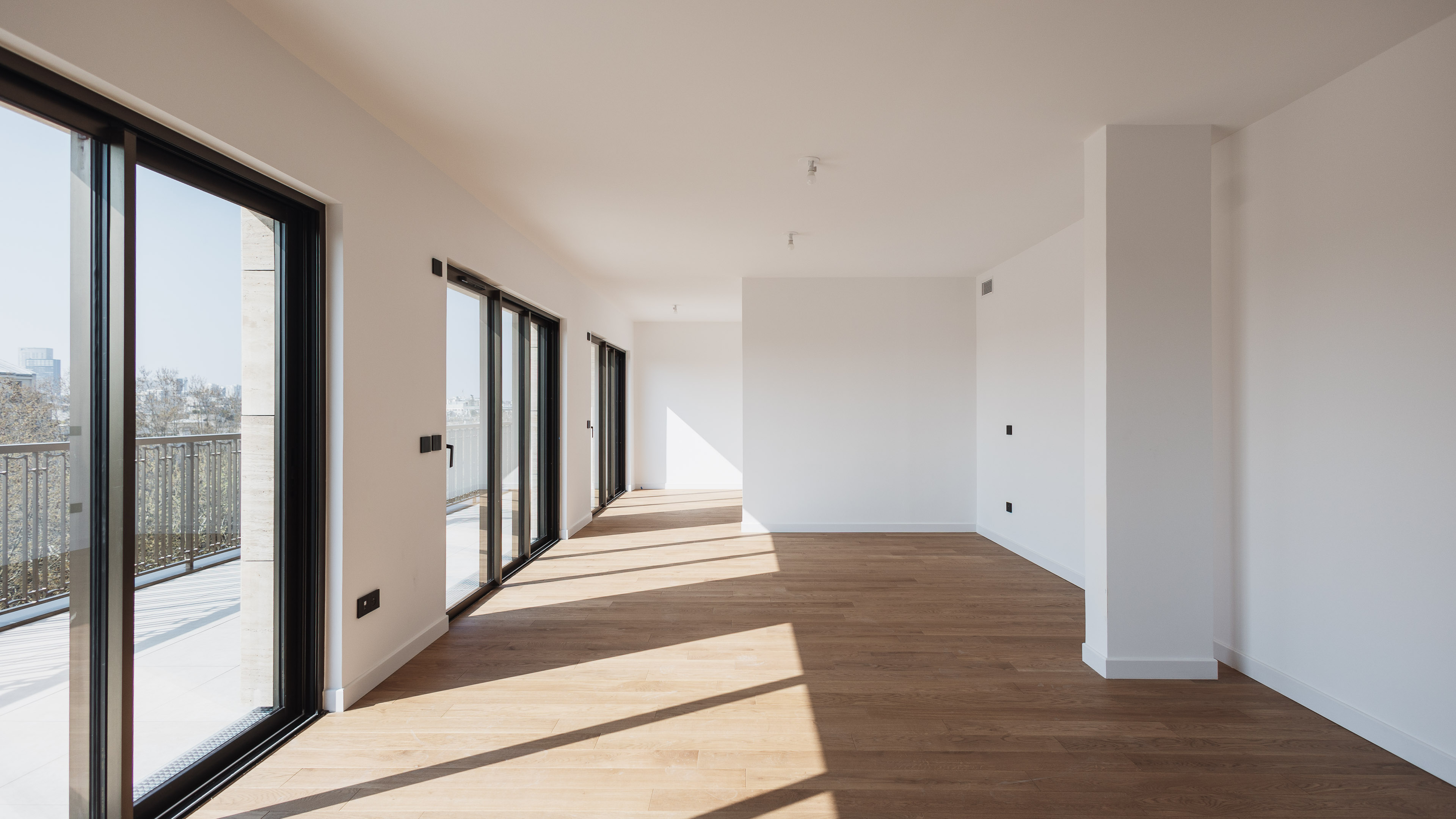 Salon lumineux d'un appartement de luxe &agrave; Paris avec parquet en ch&ecirc;ne massif et grandes baies vitr&eacute;es ouvrant sur un balcon filant par maxime decarsin photographe