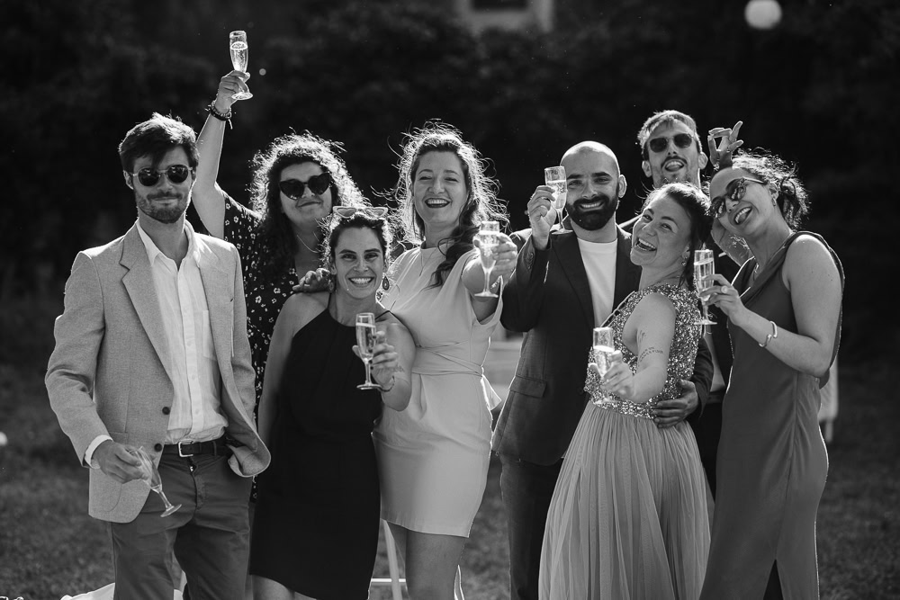Un groupe d'amis levant des coupes de champagne en train de sourire lors d'un mariage par Maxime Decarsin photographe nomade